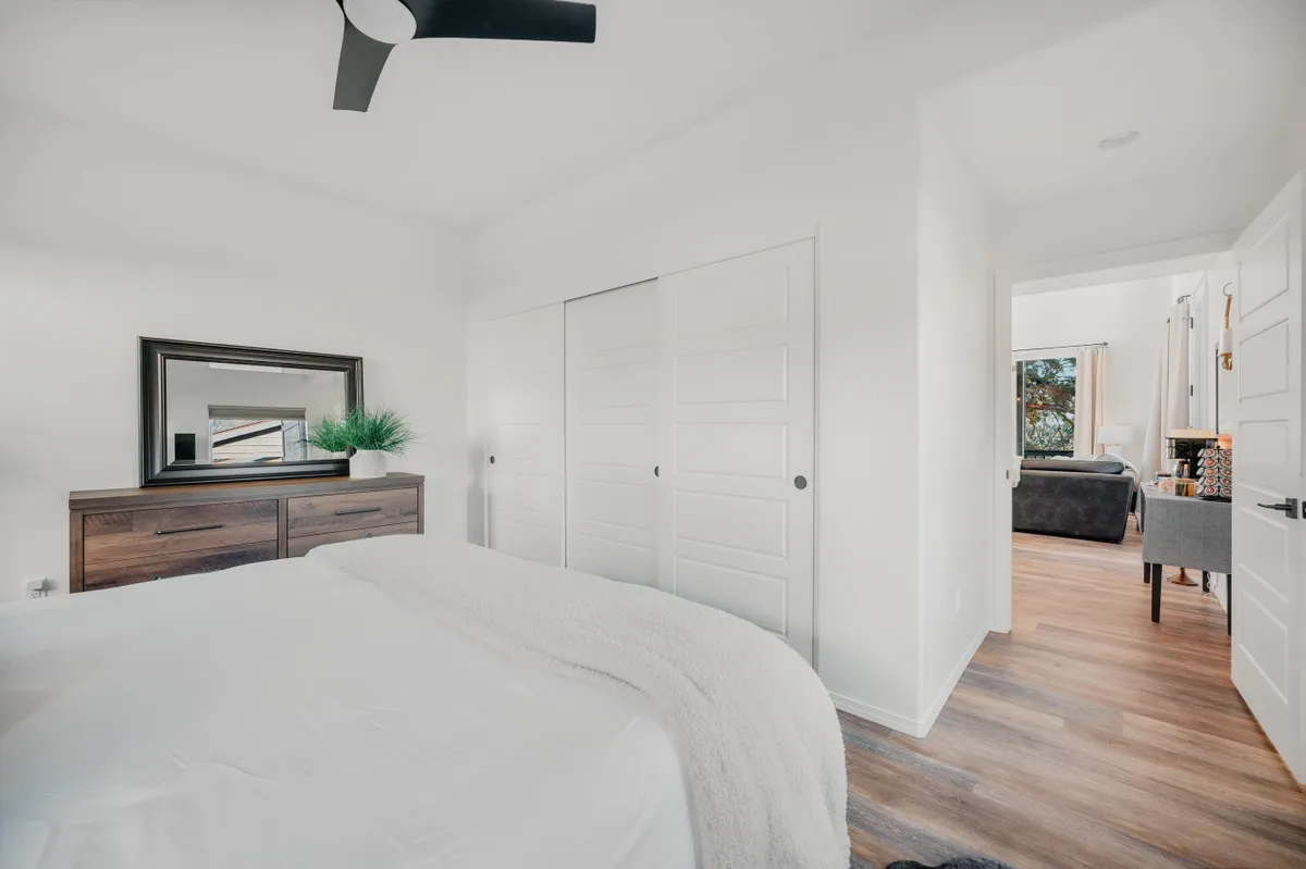 A tranquil bedroom with a neatly made bed, dresser and mirror, and a doorway leading to another room. The soft lighting creates a peaceful, restful mood ideal for relaxing or getting a good night’s sleep.
