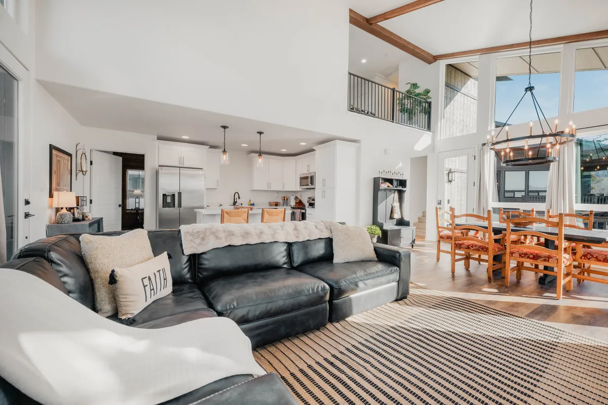 This image captures an open-concept living and dining space featuring a leather sectional couch, large windows with natural light, a wooden dining table with chairs, and stylish pendant lights. The setup is ideal for group interactions and highlights the comfort and communal aspects of the property.