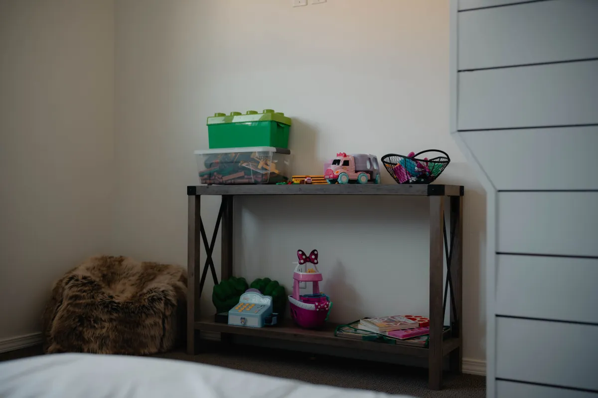 A bright and cheerful play area featuring a wooden shelf with colorful storage bins, a plush stuffed animal, and a variety of toys neatly arranged for easy access. The setting exudes warmth and is clearly designed for imaginative play and bonding between children and parents.