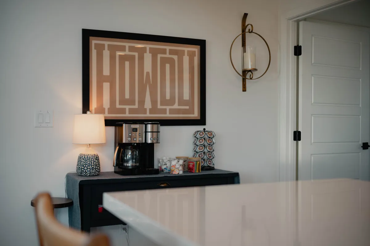 A cheerful nook with a coffee maker, 'HOWDY' artwork, a table lamp, and decorative items, capturing the spirit of friendly hospitality and relaxed mornings. The scene is bright and welcoming, hinting at the comforts awaiting before or after a day out.