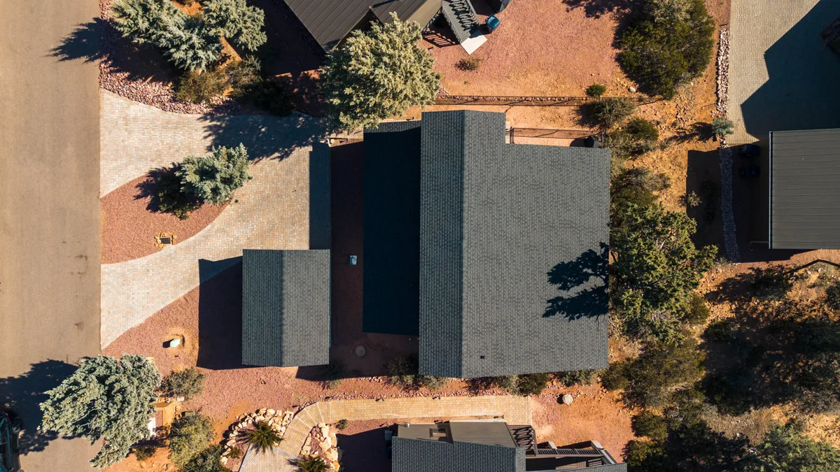 This exterior shot captures the main house set against a serene natural landscape, complete with a driveway and patio area. The view suggests ample outdoor space for gatherings, stargazing, and relaxation, fitting the description of alfresco BBQs and tranquil evening moments.