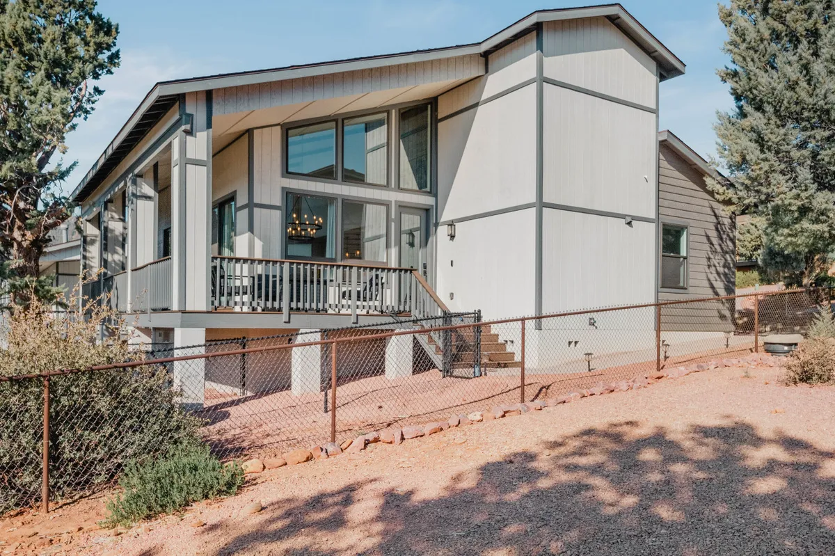 The image features a charming home exterior with large windows, a front porch, landscaped yard, and visible fencing. The welcoming porch and fenced yard suggest a safe area for children to play and for families to gather outdoors.