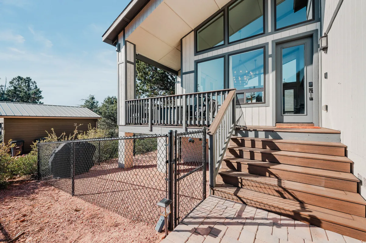 An exterior view showing the home’s front steps, a sturdy fence, large windows, and a welcoming deck area, hinting at the fully fenced side yard where children can play safely outdoors while parents relax nearby.