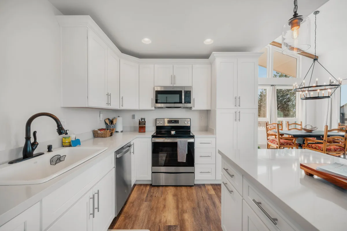 A bright, open kitchen area with white cabinetry, stainless steel appliances, large windows, and an adjacent dining area. The layout is functional and sociable, ideal for group meals and celebrations.