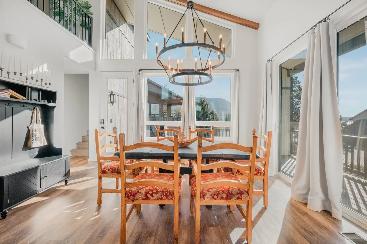 A cozy dining area with a central table, a chandelier overhead, and large windows letting in natural light. The setting is inviting for shared meals, celebrations, and casual conversations.