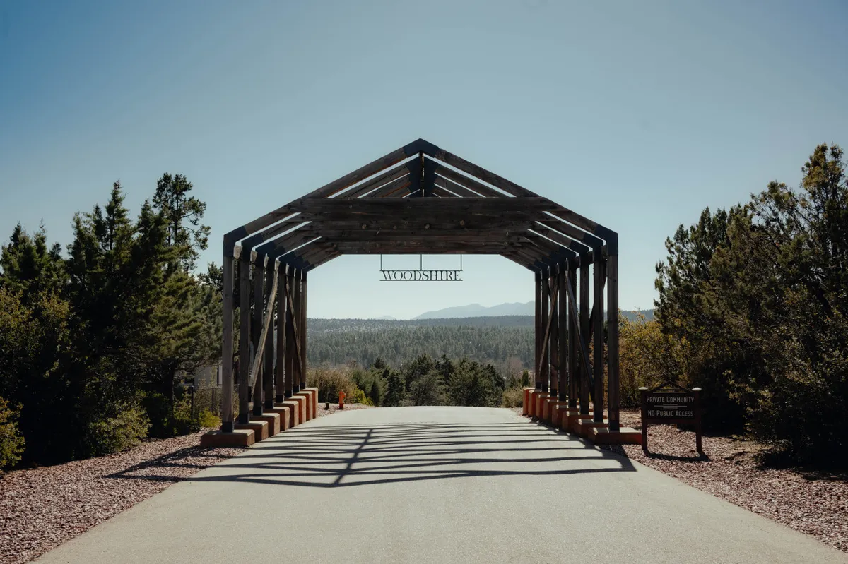 This exterior shot captures a wooden archway leading to a scenic mountain view, surrounded by lush trees. The inviting path encourages outdoor exploration and hints at the natural beauty and adventure available within the gated community.