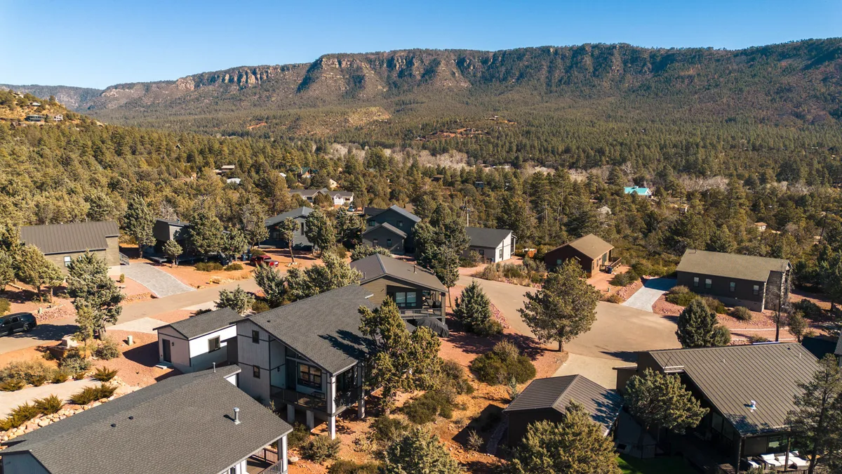 An exterior scene with a cluster of houses set among lush green trees, framed by mountains in the background. The peaceful setting invites outdoor activities like hiking and nature walks, with ample opportunities for stargazing and wildlife observation.