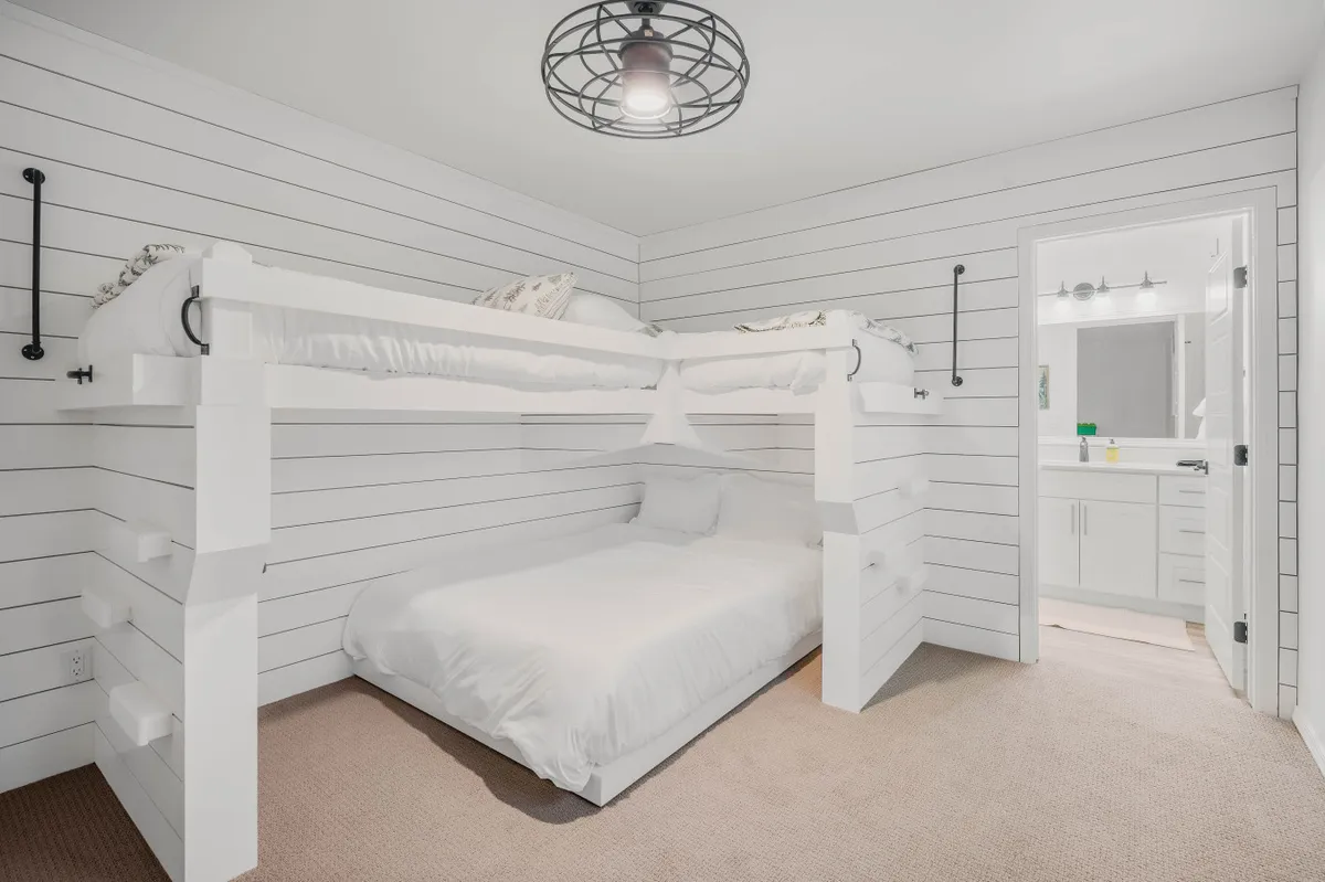 A cozy bedroom with a playful bunk bed, white walls, and a view through to an adjoining bathroom. The space is inviting and designed for children, offering a sense of adventure and comfort for sleepovers or family stays.
