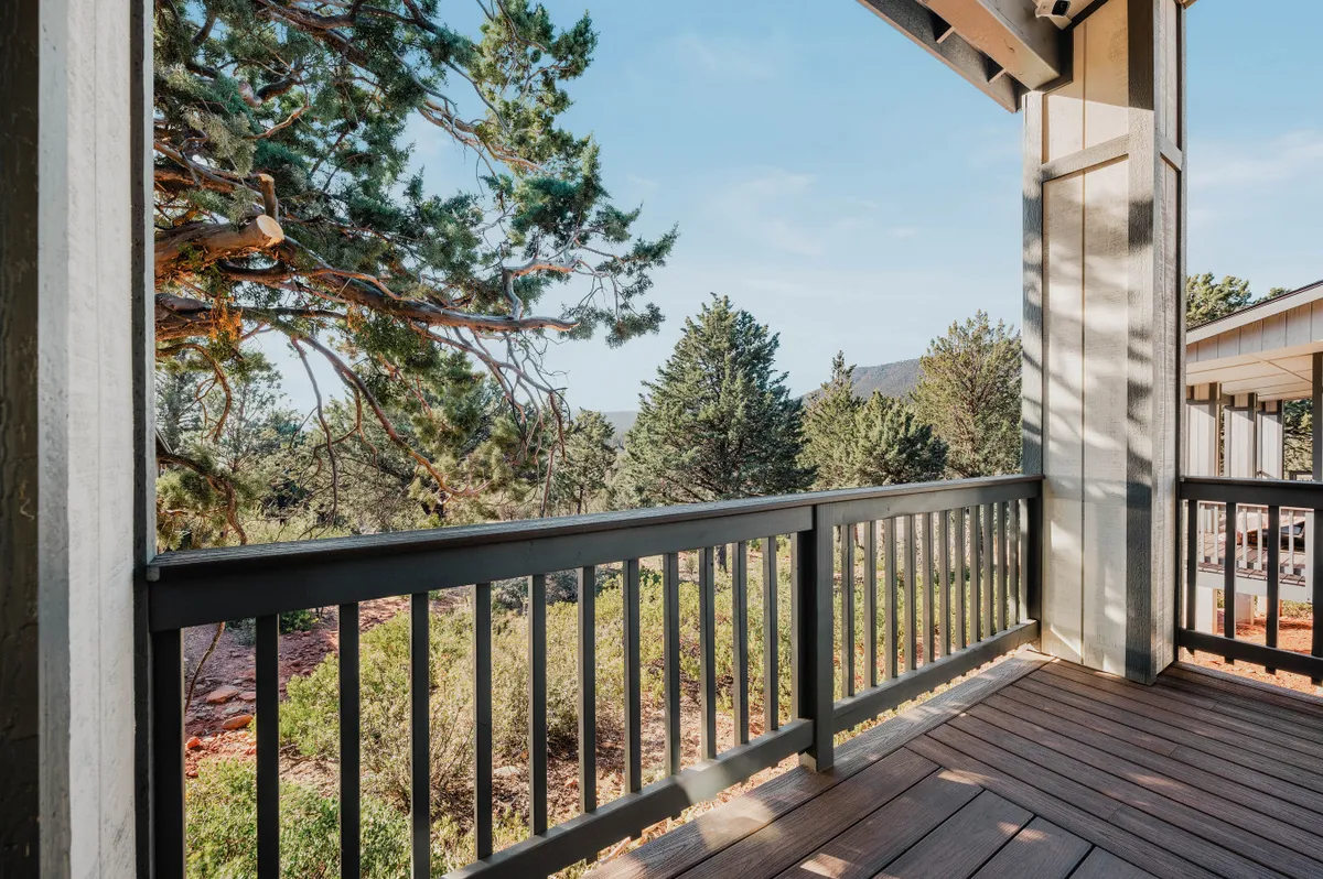 The image features a wooden deck railing overlooking lush green trees and distant mountains. The view highlights the sense of serenity and connection to nature, with the deck itself suggesting a perfect spot for morning coffee or sunset relaxation.