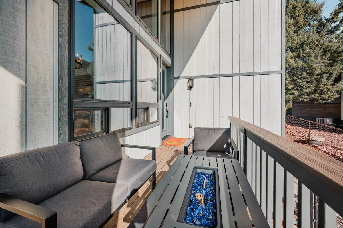 This image showcases an inviting outdoor seating area centered around a fire pit, with a textured wall and outdoor railing visible. The arrangement suggests a comfortable space for socializing, enjoying the warmth of the fire, and taking in the surrounding natural light.