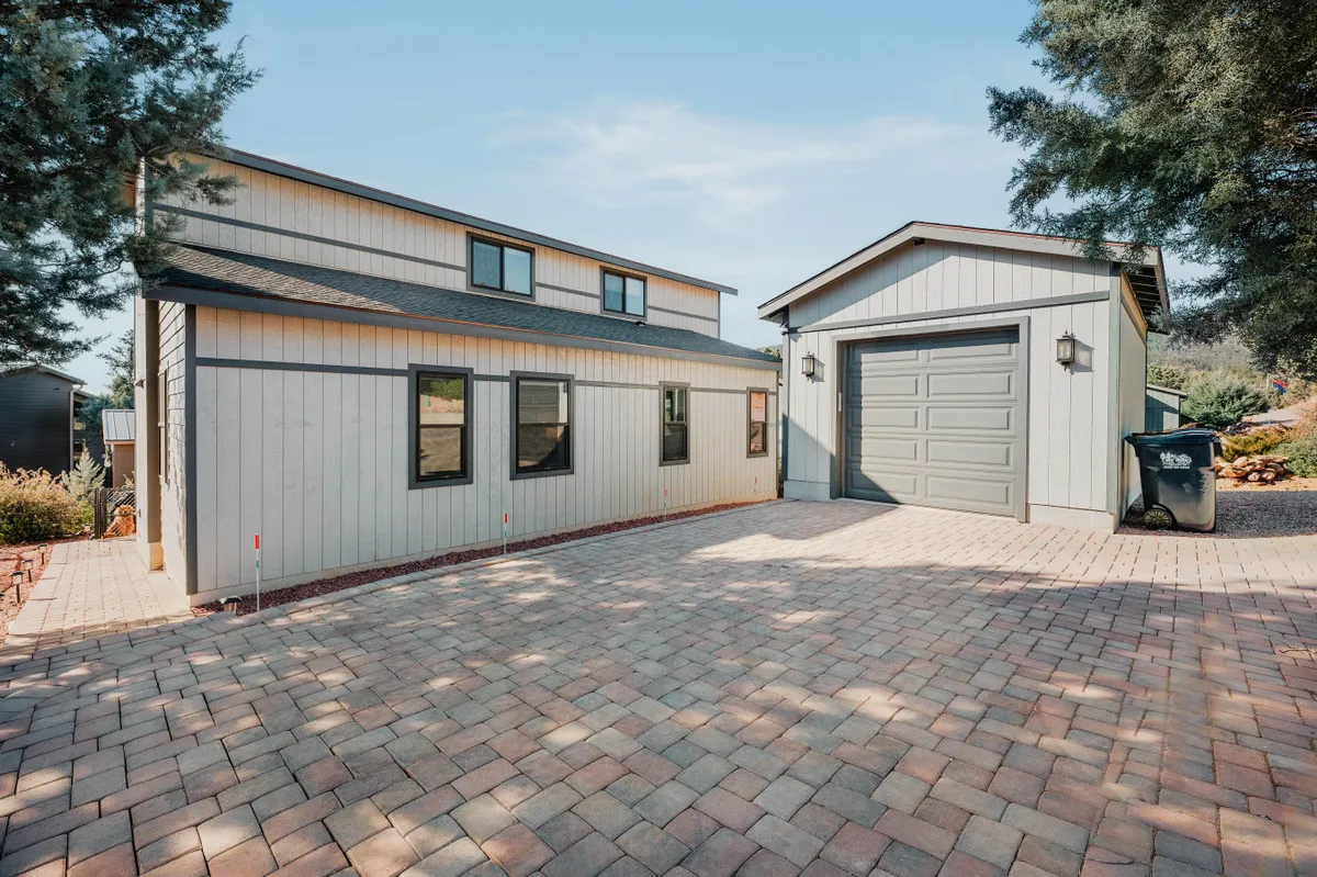 An inviting view of a two-story house with a garage and paved driveway, set against a pleasant outdoor backdrop. The open yard space suggests room for children to play, family barbecues, and group activities.
